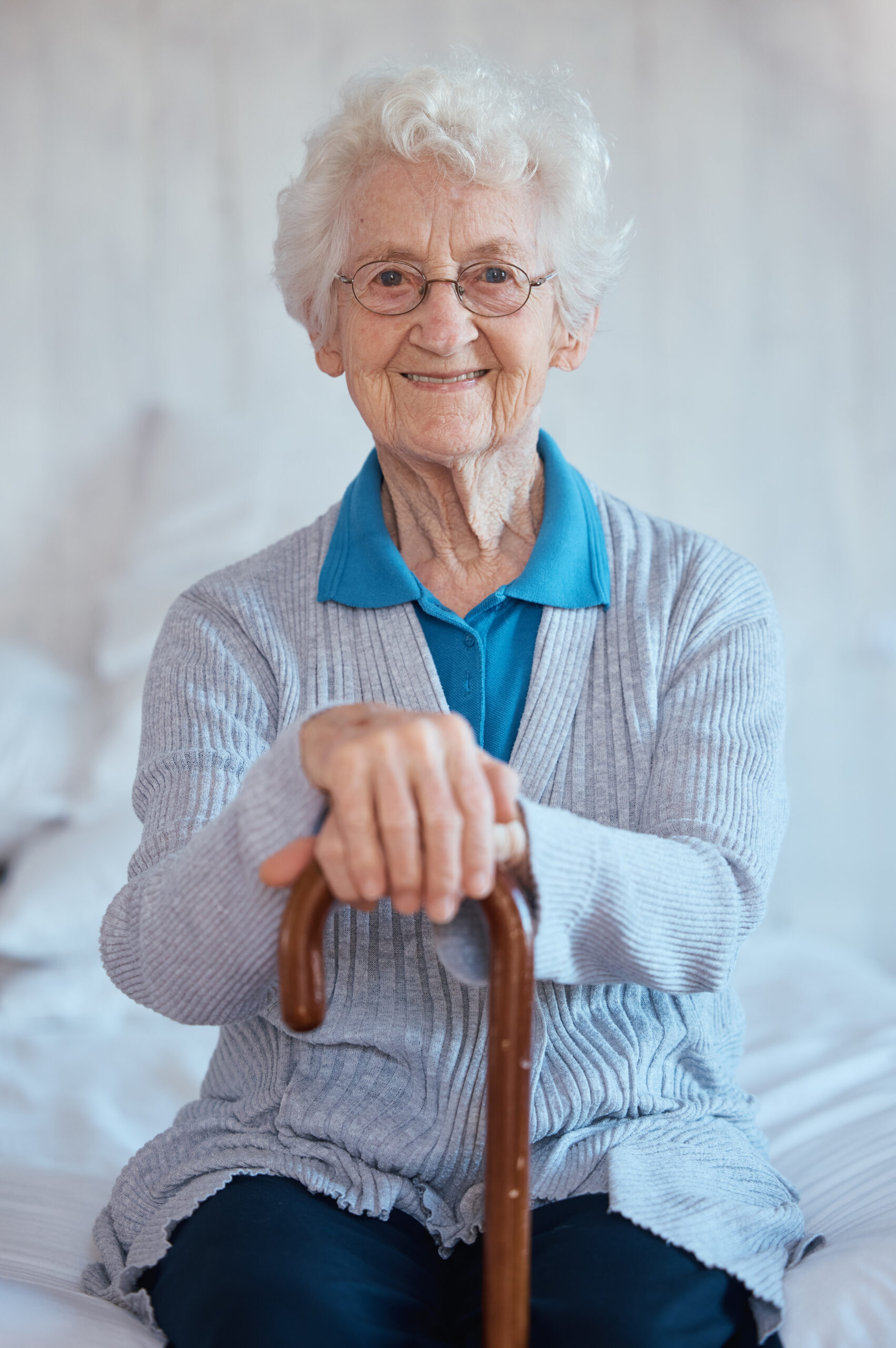 Elderly woman, sitting portrait and smile on bed with happiness, walking stick and relax in nursing home. Happy senior lady, bedroom and cane for support, healthcare and wellness in retirement house
